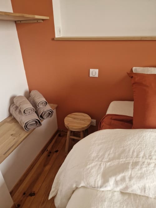 Chambre accueillante à la Maisonaurinko B&B à Thenon avec murs en terre cuite, lit en bois, serviettes roulées et tabouret en bois.