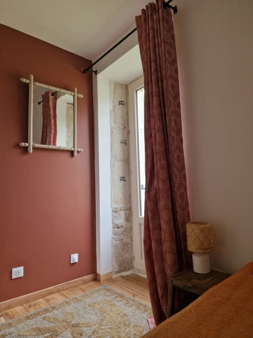 Chambre de la Maison Aurianko à Thénon avec murs couleur rouille, miroir, rideaux et parquet