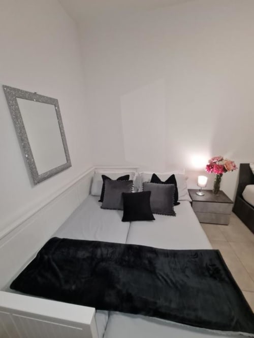 Moderna spavaća soba u apartmanu Raymihome Turin s bijelom posteljinom, crnim jastucima, sivim zrcalom, noćnim ormarićem s ružičastim cvijećem