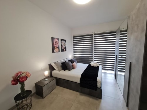 Camera moderna dell'hotel Raymihome a Torino con letto queen, persiane a righe, rose rosa e arredamento minimalista
