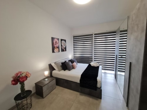 Moderna spavaća soba u apartmanu Raymihome Turin s bračnim krevetom, crnim prugastim žaluzinama, cvjetnim zidnim umjetnostima i suvremenim dizajnom
