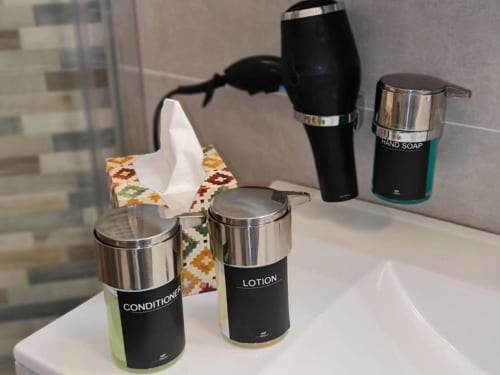 Kupaonski pribor u apartmanu Raymihome u Torinu: kondicionator, losion, tekući sapun, sušač za kosu i maramica na bijelom pultu