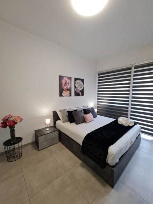 Moderna spavaća soba u apartmanu Raymihome Torino s tamnim krevetom, prugastim žaluzinama, cvetnim umetničkim delom i ružičastom noćnim stoliću