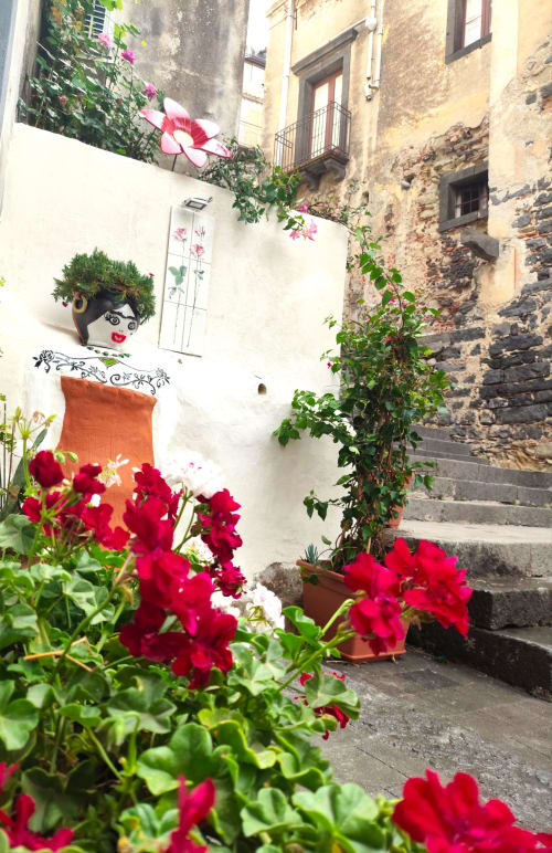 Incantevole cortile di Casa Fiore del Borgo con vivaci petunia rosse e simpatico vaso-viso a Castiglione di Sicilia