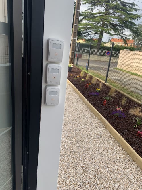 Trois capteurs de mouvement blancs montés sur la façade extérieure de La Maison Blanche B&B, Bouguenais, avec jardin et clôture visibles