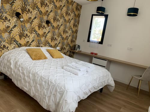 Camera moderna a La Maison Blanche B&B a Bouguenais con letto trapuntato bianco, cuscini dorati e carta da parati floreale