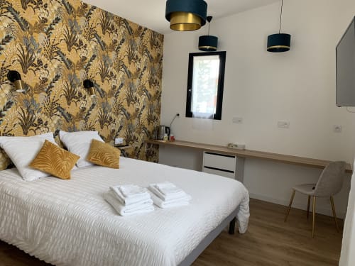 Chambre moderne à La Maison Blanche B&B à Bouguenais avec mur d'accent aux motifs dorés, lit blanc et luminaires suspendus