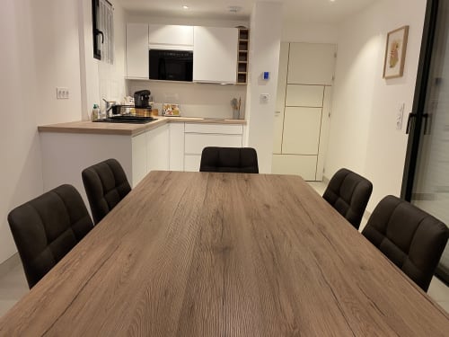 Élégante salle à manger avec table en bois et chaises noires, cuisine blanche au fond, La Maison Blanche BnB Bouguenais