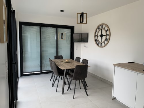 Salle à manger moderne de la Chambre d'hôtes La Maison Blanche à Bouguenais avec table en bois, chaises noires et larges portes vitrées