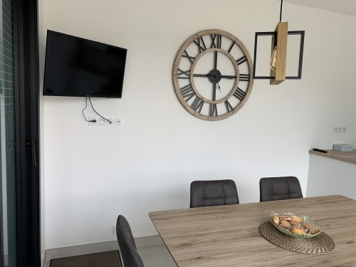 Salle à manger moderne du gîte La Maison Blanche à Bouguenais avec table en bois, chaises noires, horloge murale et télévision