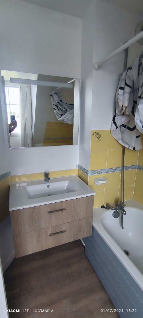 Salle de bains moderne de l'appartement Loc'Maria avec vasque, miroir, carrelage jaune et baignoire-douche