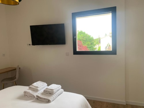 Camera moderna presso La Maison Blanche B&B con TV a schermo piatto, asciugamani freschi sul letto e finestra con vista sul giardino di Bouguenais