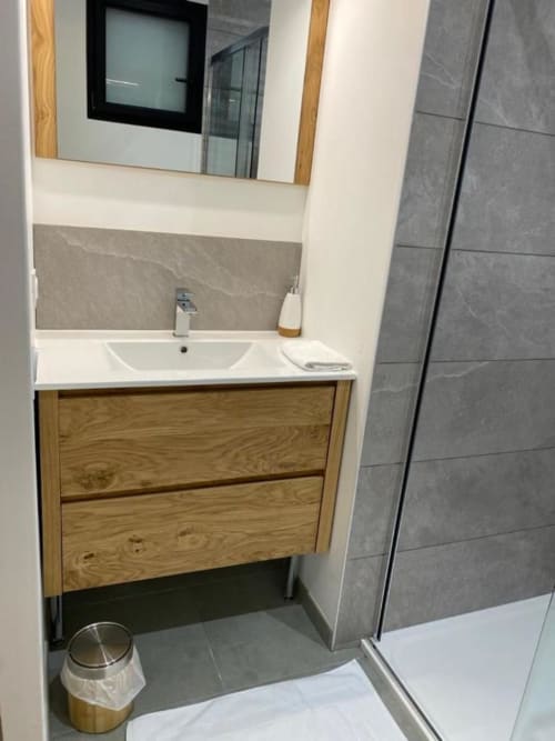 Bagno moderno con mobile in legno, lavabo bianco e pareti piastrellate grigie presso La Maison Blanche B&B, Bouguenais