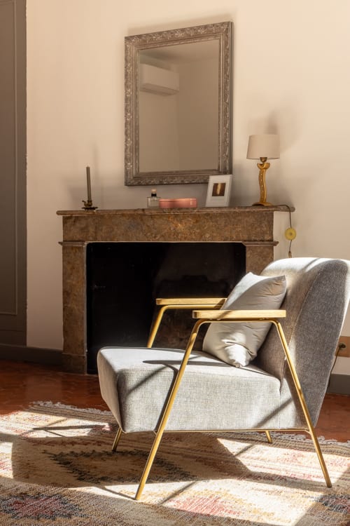 Elegant fireplace seating area in Madeleine Room at Le Prieuré Notre-Dame with beige armchair, ornate mirror, and warm