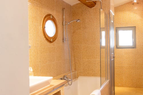 Modern bathroom with orange mosaic tile walls, bathtub, walk-in shower, and circular mirror at Le Prieuré Notre-Dame,