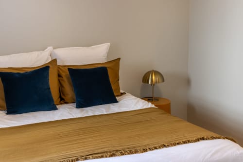 Chambre Alphonse au Prieuré Notre-Dame à Montfrin avec lit habillé, coussins bleu marine, lampe en laiton et décoration neutre