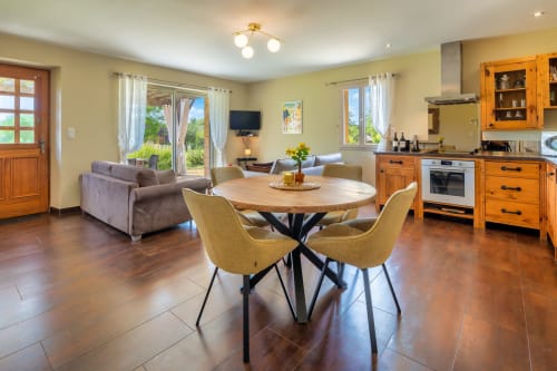 Lichte open eetruimte met ronde houten tafel, gele stoelen, keuken en woonruimte op Domaine De Campagnac