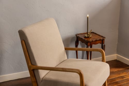 Cream armchair with wooden frame beside side table with lit candle at Le Prieuré Notre-Dame boutique hotel in Montfrin