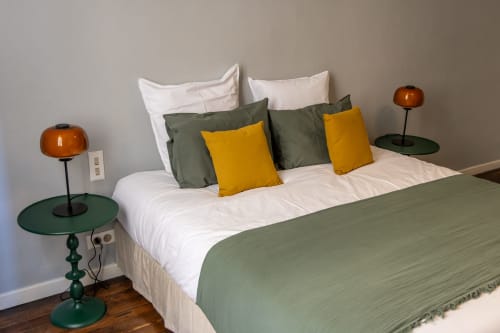 Modern bedroom at Le Prieuré Notre-Dame in Montfrin with white linens, green and gold pillows, copper lamps, and dark wood