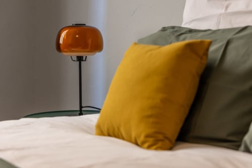 Modern bedroom at Le Prieuré Notre-Dame with yellow pillow, ambient orange lamp, and white bedding in Montfrin