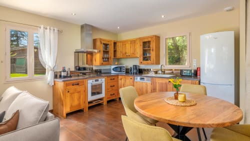 Lichte open keuken-eetkamer met houten kasten, eettafel en uitzicht op de tuin in het cottage Domaine De Campagnac.