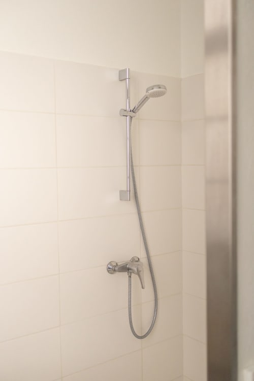 Modern shower setup with handheld showerhead and metal fixtures in Le Prieuré Notre-Dame bathroom