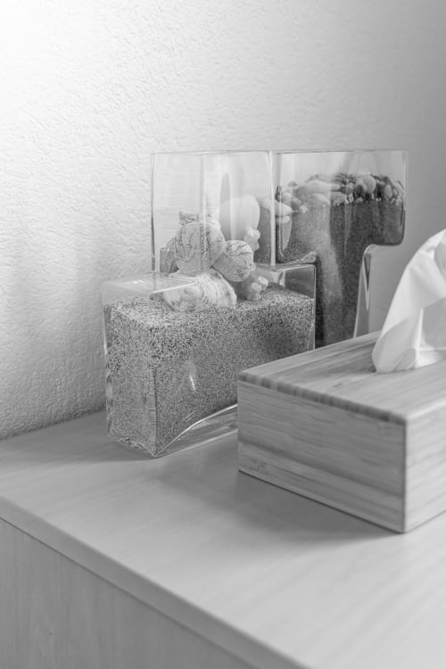 Bathroom amenities at Le Prieuré Notre-Dame, Montfrin: glass dispenser with sand and white toiletries beside wooden tissue