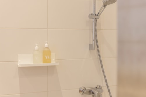 Modern shower setup at Le Prieuré Notre-Dame in Montfrin with amenity shelf and rainfall showerhead