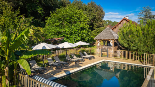 Tuinaanzicht van Domaine De Campagnac met verwarmd zwembad, ligbedden, parasols en houten cottage in Carsac-Aillac