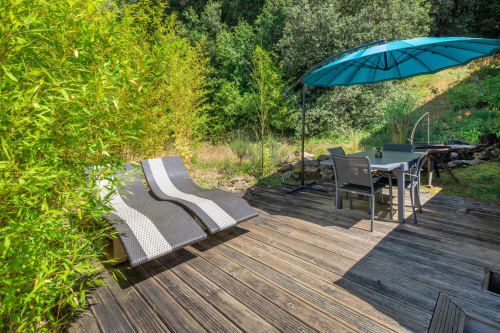Buitenterras van cottage Domaine De Campagnac met ligstoelen, blauwe parasol en eetgedeelte omgeven door groen