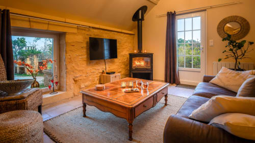 Gezellige woonkamer in Domaine De Campagnac met open haard, houten tafel, leren zitplaatsen en tuinzicht