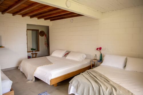 Luminoso dormitorio de villa en Olamar Living con dos camas de madera, ropa blanca, vigas expuestas y vistas al mar en Santiago de Tolú