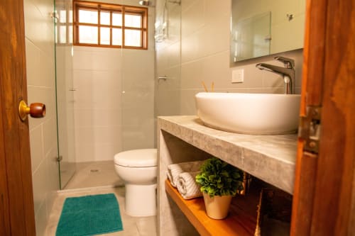 Baño moderno con lavabo tipo recipiente, ducha de vidrio y detalles de madera en la villa Olamar Living en Santiago de Tolú, Colombia