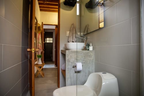 Baño moderno en villa Olamar Living en Santiago de Tolú con lavamanos de cerámica, inodoro y paredes con azulejos grises