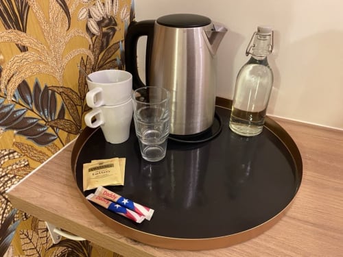 Vassoio di benvenuto presso La Maison Blanche B&B con bollitore, tazze, bicchieri, tè e acqua in bottiglia su tavolo nero