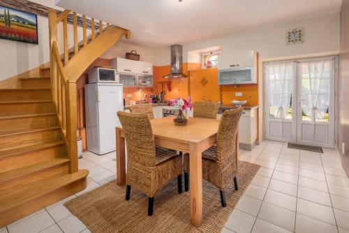 Moderne keuken en eetkamer met houten tafel, geweven stoelen en oranje accentmuur bij Domaine De Campagnac