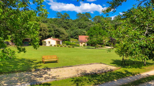 Weelderige tuinen van Domaine De Campagnac B&B in Carsac-Aillac met houten bank, verzorgd gazon en cottage's omgeven door bomen