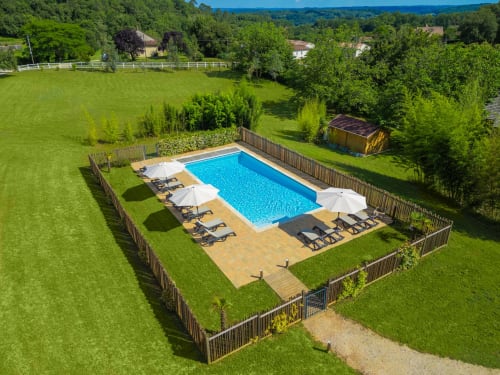 Domaine De Campagnac rectangular swimming pool with loungers and umbrellas surrounded by green gardens in Carsac-Aillac