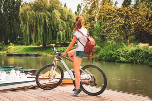 Femme à vélo sur un quai du Marais poitevin au bord de l'eau avec barques, arbres, en Nouvelle-Aquitaine