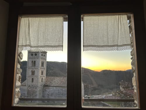 Vista de la torre de la iglesia desde la habitación de Casa Tapiolas en Molló, Girona al atardecer con los Pirineos y cortinas de encaje
