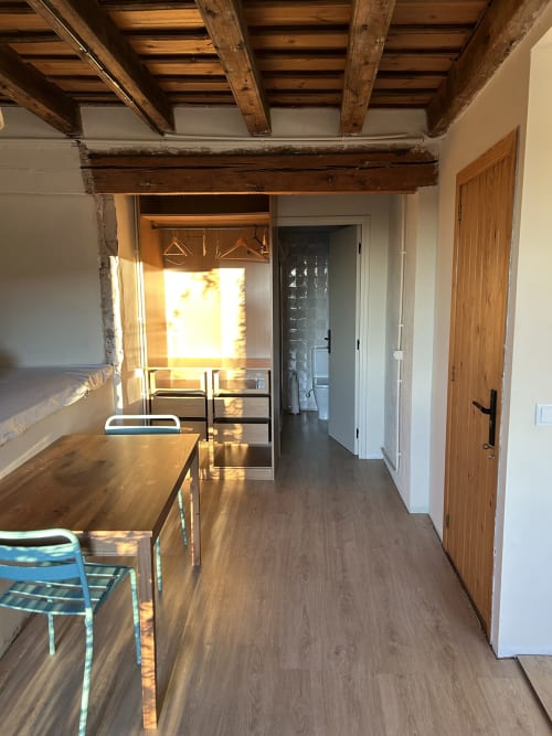 Habitación SENGLAR en Casa Tapiolas de Molló con vigas de madera vista, mesa de madera, zona de estar y puertas de cristal con vistas emblemáticas