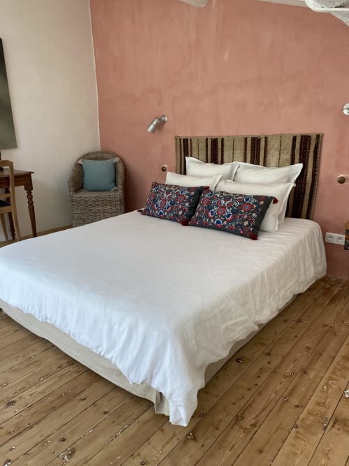 Chambre au Mas du Fort à Gargas : linge blanc, tête de lit rayée, coussins décoratifs, fauteuil en rotin, touches terracotta