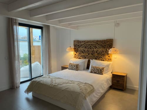 Quarto espaçoso com vista para o mar na Casa Furnas, Bordeira. Cabeceira em madeira entalhada, luminárias pendentes e acesso ao terraço.