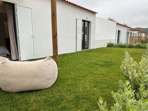 Quintal da villa Casa Furnas com gramado verdejante, poltrona tipo puff branca e vistas para o mar em Bordeira, Portugal