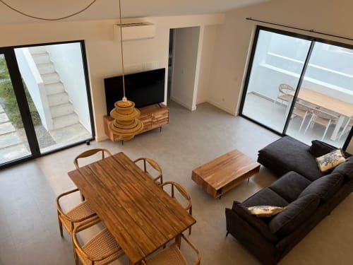 Sala de estar moderna da villa com mesa de jantar em madeira, sofá preto, TV e portas de vidro que abrem para o terraço da Casa Furnas