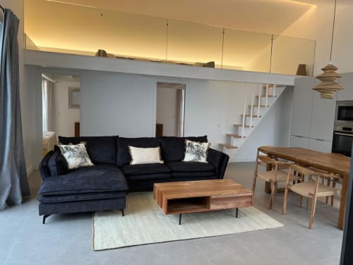 Sala de estar em conceito aberto da villa Casa Furnas com sofá secional preto, mesa de jantar em madeira e cozinha com vista ao mar