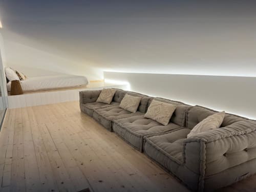 Quarto mezzanino moderno com cama integrada, sofá modular cinzento, piso de madeira e iluminação ambiente na villa Casa Furnas