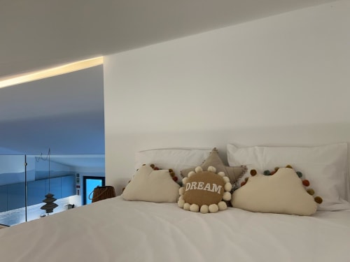Quarto elegante com almofadas brancas e almofadinhas decorativas na villa Casa Furnas, Bordeira, com vista para o mar através de parede de vidro