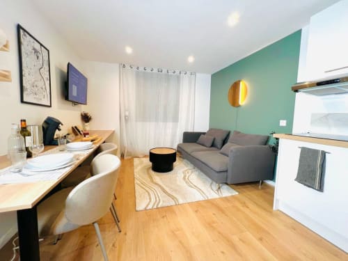 Modern apartment living area in Bordeaux with gray sofa, dining table, kitchenette, and green accent wall at Wellkhome