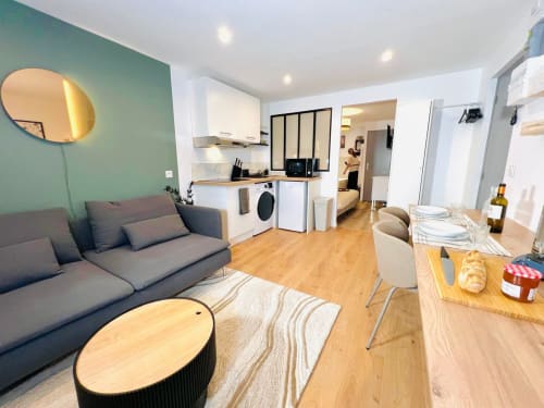 Modern studio apartment in Bordeaux with gray sofa, equipped kitchen, wooden dining table, and teal accent wall